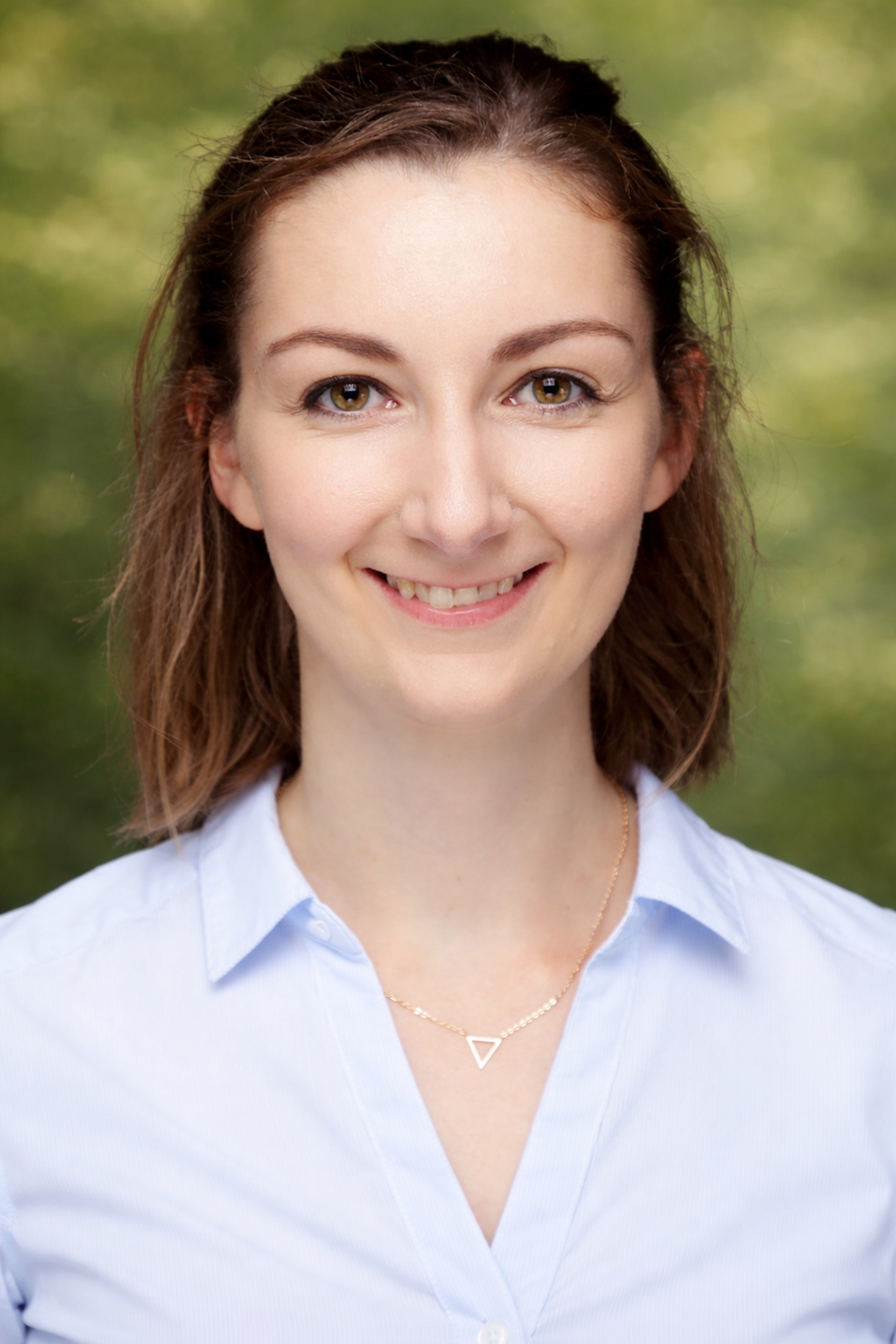 Porträtbild einer jungen Frau in weißer Bluse mit dünner Goldkette um den Hals, schulterlangen hellbraunen Haaren und hellbraunen Augen; sie lacht in die Kamera