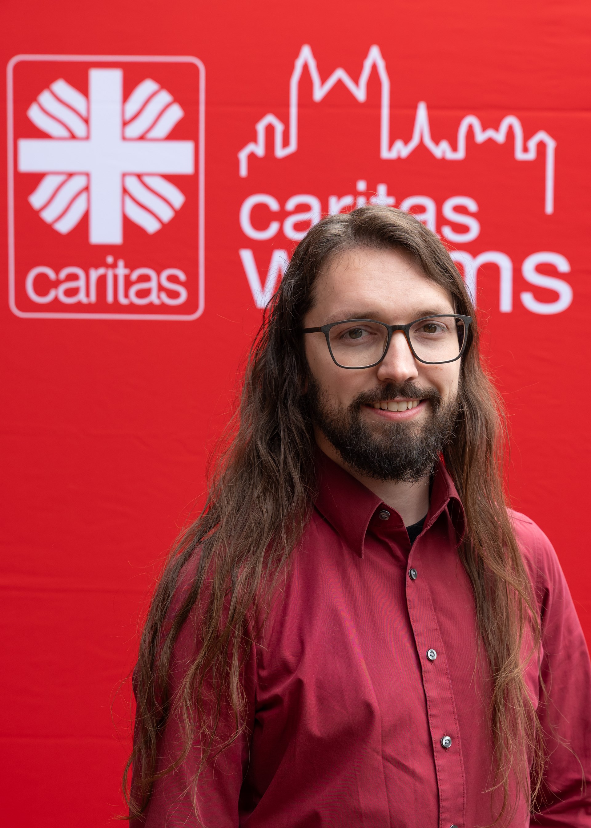 junger Mann mit dunklen langen Haaren, Brille und rotem Hemd