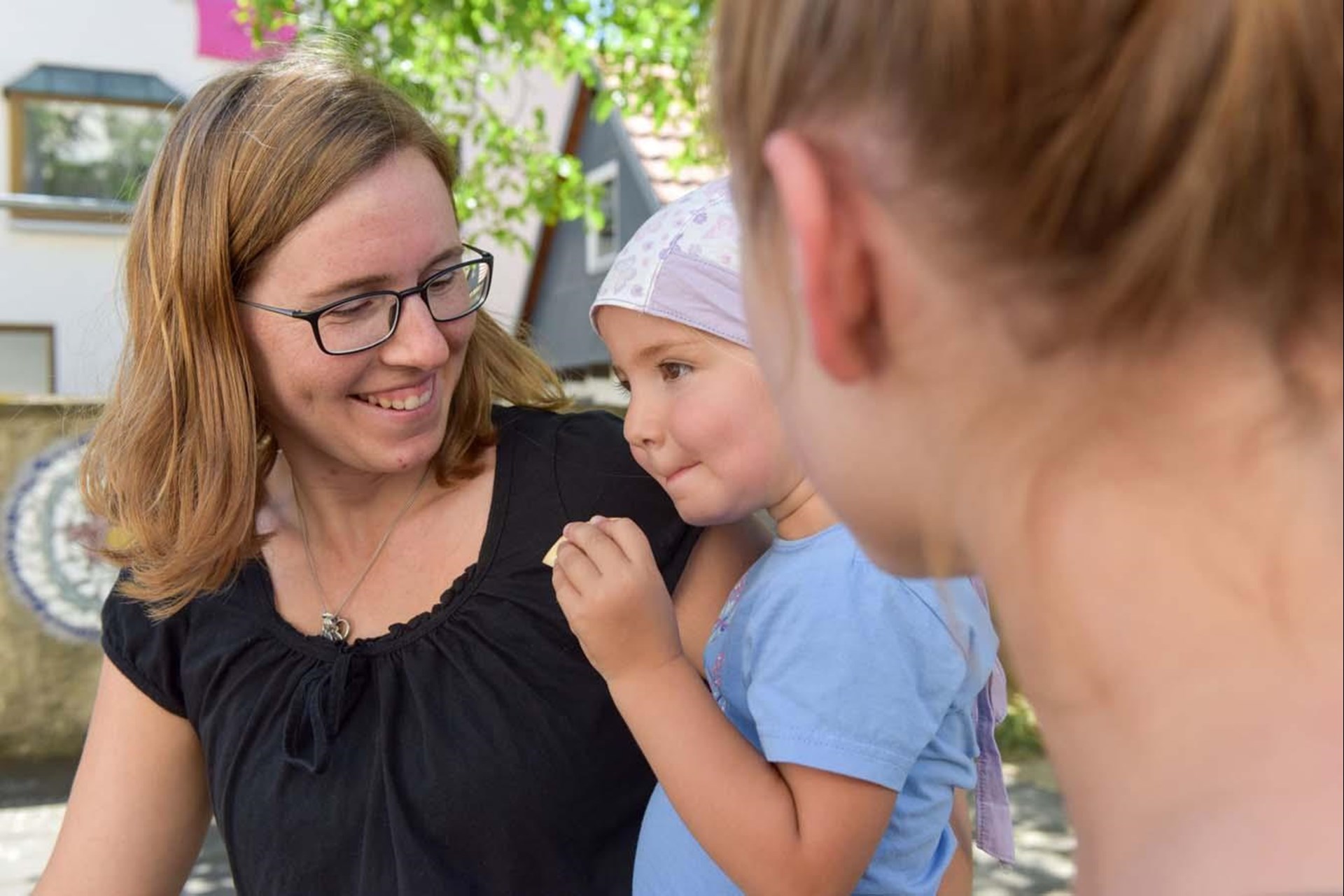 Mutter und Kita-Erzieherin schauen Tochter auf dem Arm der Mutter an