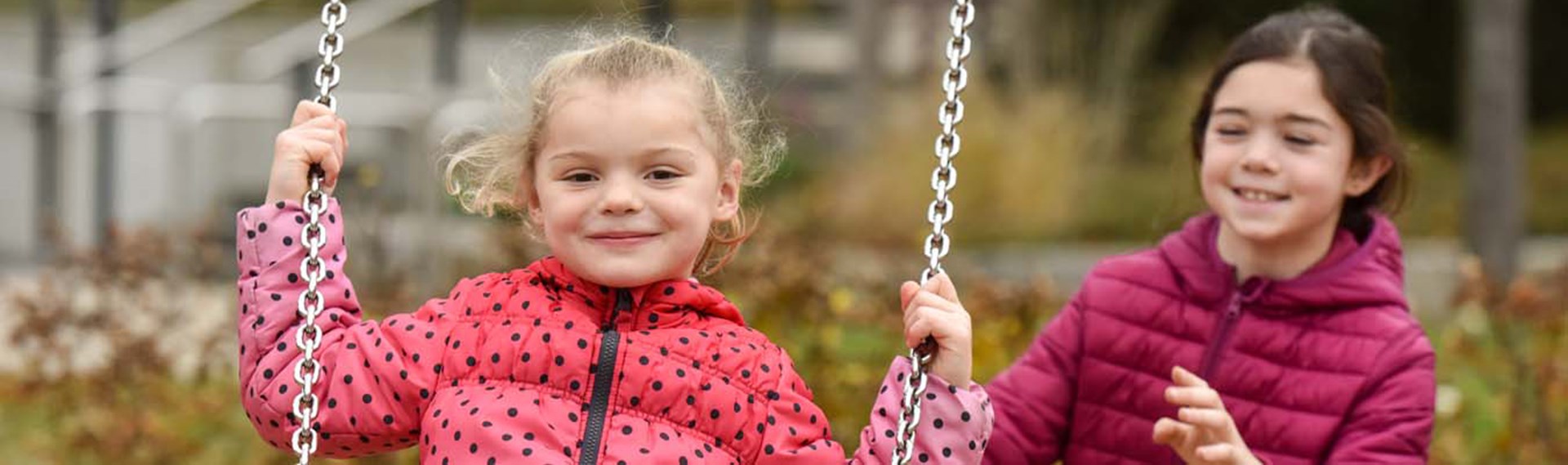 Ein kleines Mädchen schuckt ein anderes auf der Schaukel an