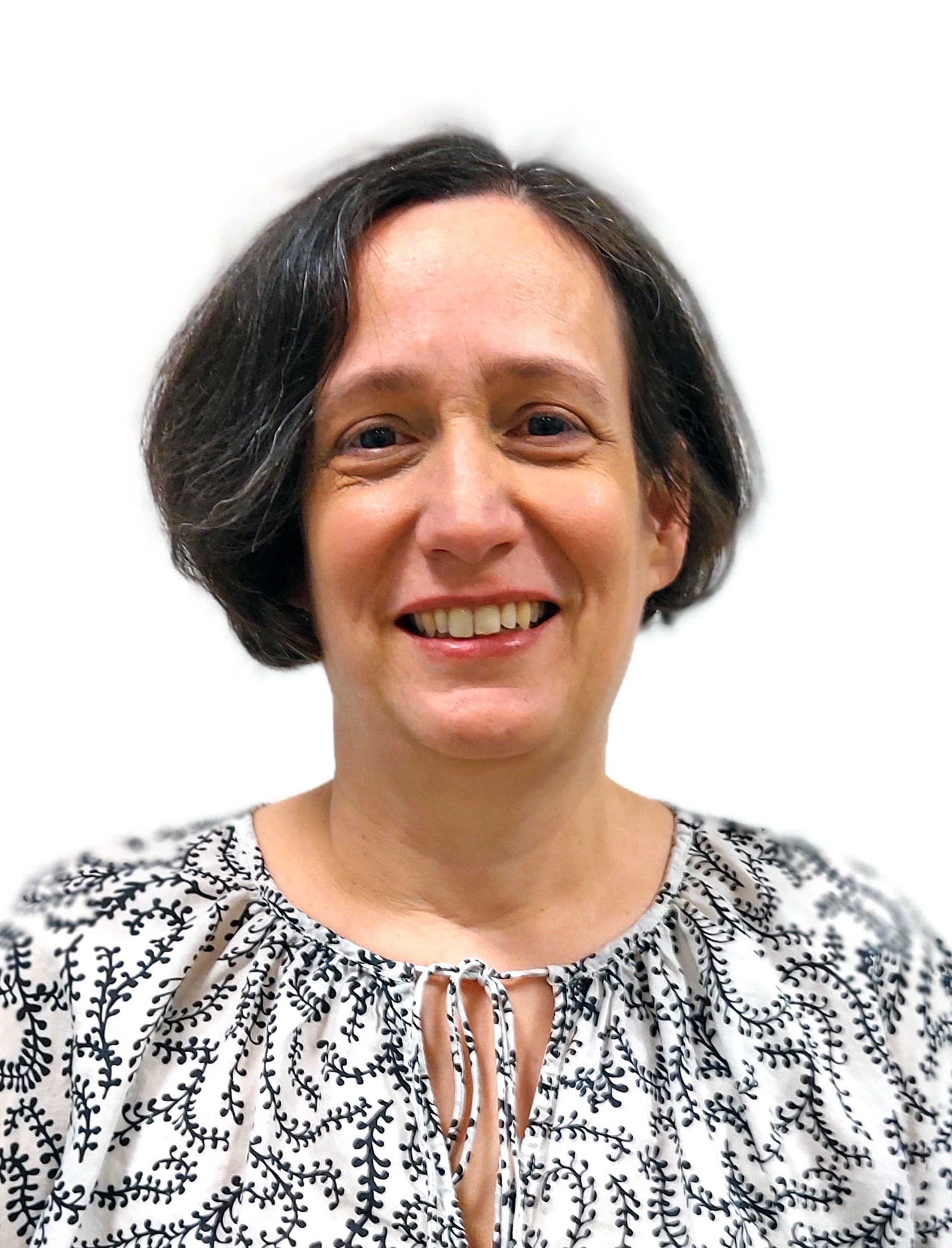 Porträt einer lächelnden Frau mit kurzem dunklem Haar vor hellem Hintergrund, sie trägt eine helle Bluse mit dunklem Pflanzenmuster.