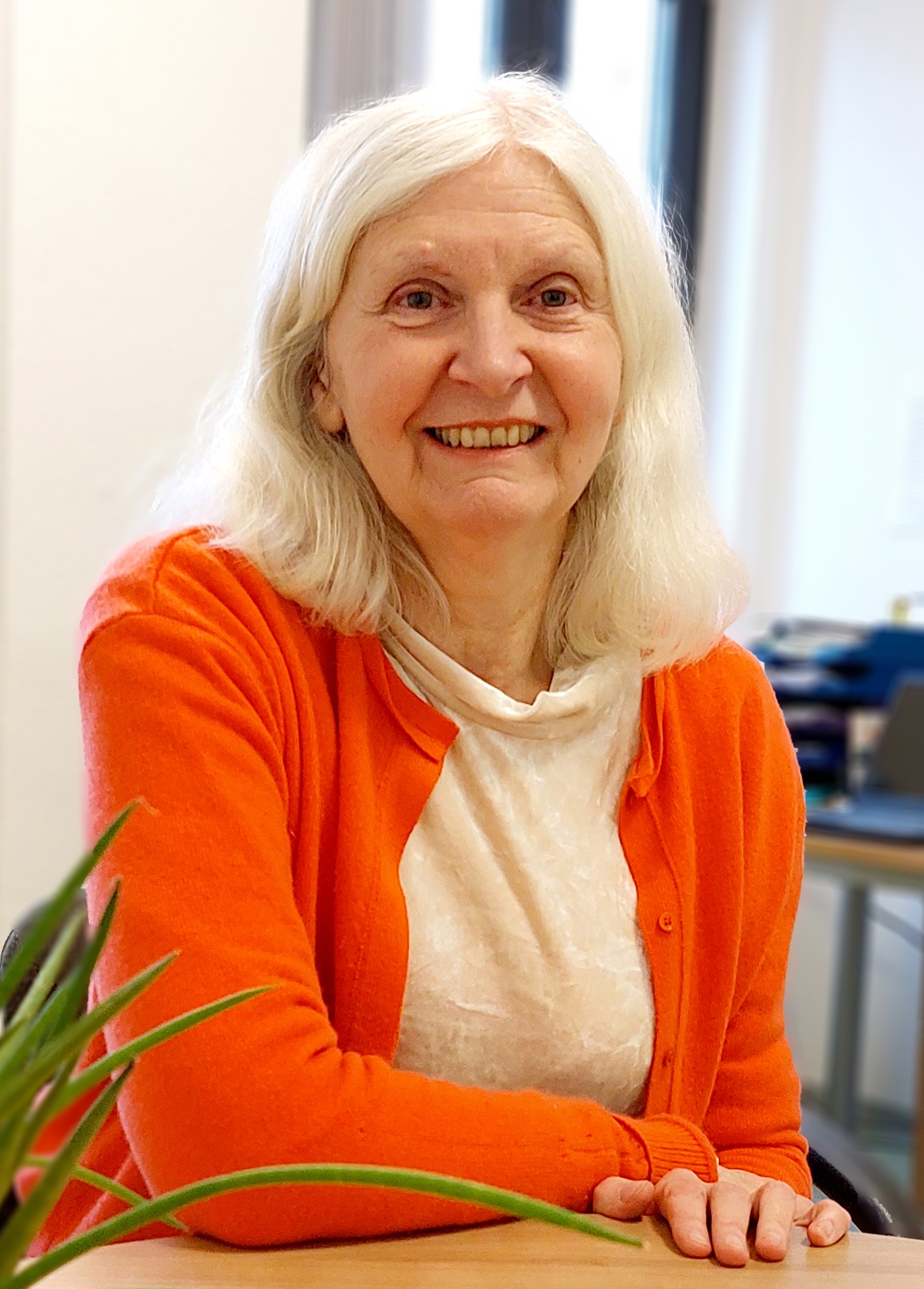 Halbporträt; eine Frau mit langen grauen Haaren und rotem Pullover lacht in die Kamera